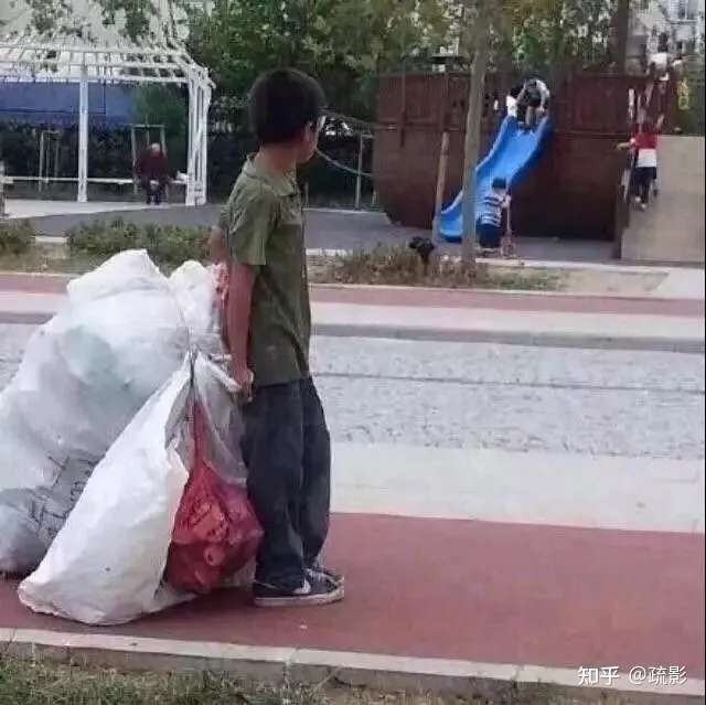 一捡破烂的小孩看着马路对面的同龄人在玩滑梯